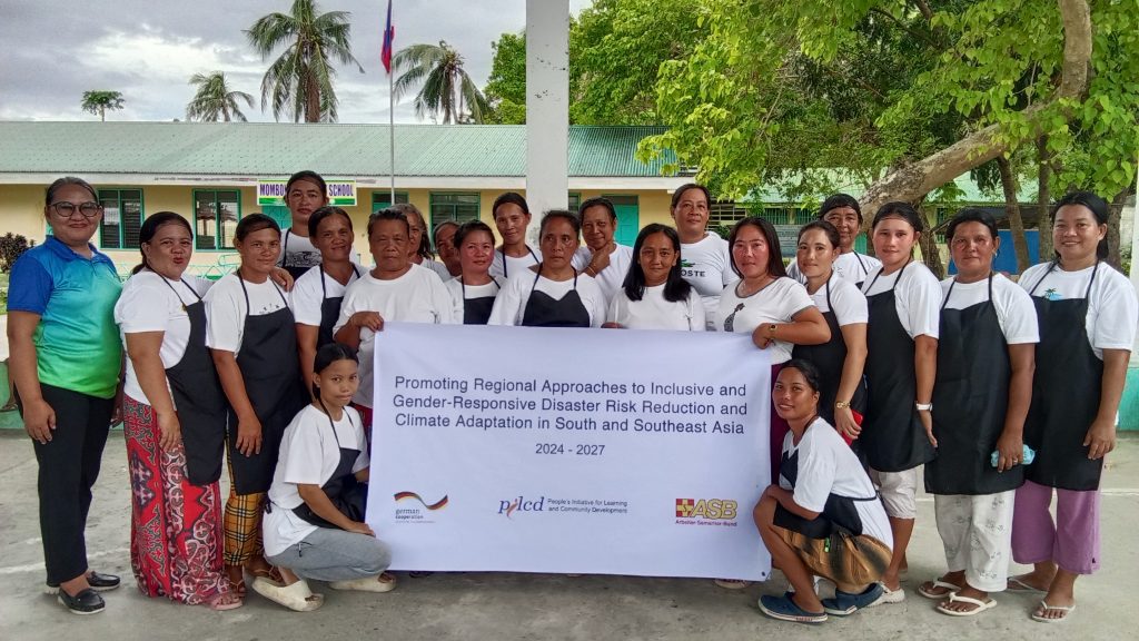 Group photo of members of the Mombon Women’s Organisation in Samar, Philippines, standing together and holding a banner for the project “Promoting Regional Approaches to Inclusive and Gender-Responsive Disaster Risk Reduction and Climate Adaptation in South and Southeast Asia (2024–2027),” implemented in partnership with ASB and supported by BMZ.