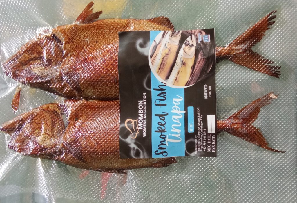 Vacuum-sealed smoked fish labeled “Mombon Women’s Association Smoked Fish (Tinapa),” displaying the group’s branding and product information as part of their livelihood enterprise.