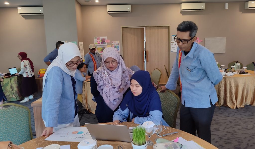ASB S-SEA team members collaborating around a table, discussing and reviewing work on a laptop during the National Team Meeting 2026.